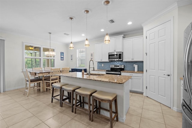 kitchen with white cabinets, hanging light fixtures, a kitchen island with sink, and appliances with stainless steel finishes