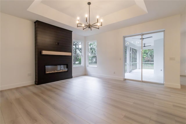 unfurnished living room featuring a fireplace, light hardwood / wood-style floors, a chandelier, and a tray ceiling