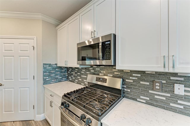 kitchen featuring stainless steel appliances, white cabinetry, ornamental molding, light stone countertops, and light wood-type flooring