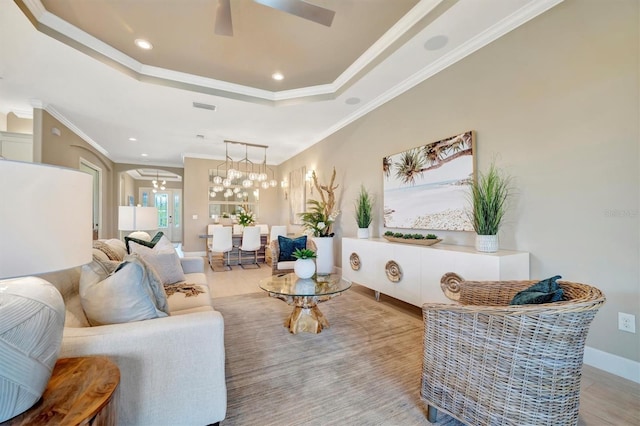 living room featuring a tray ceiling, crown molding, ceiling fan with notable chandelier, and light wood-type flooring