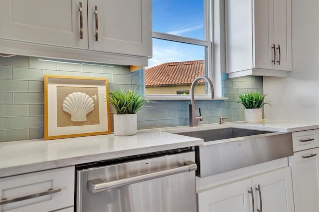 kitchen featuring decorative backsplash, light stone countertops, white cabinets, sink, and dishwasher