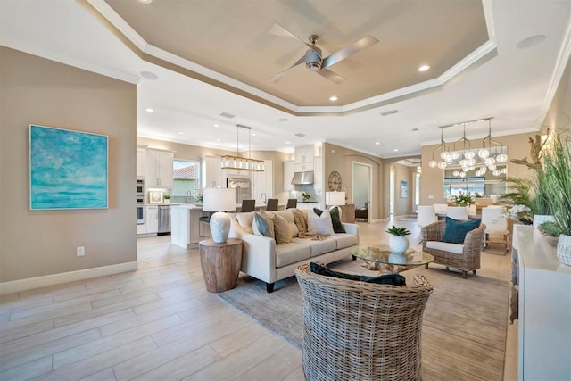 living room featuring a raised ceiling, sink, a healthy amount of sunlight, and ornamental molding