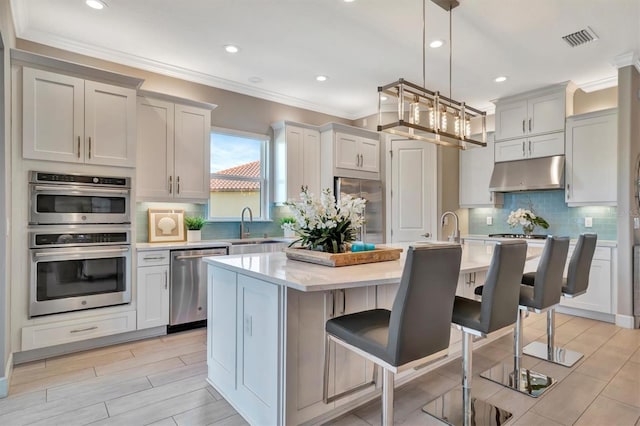 kitchen featuring decorative light fixtures, stainless steel appliances, a kitchen island with sink, and a breakfast bar area