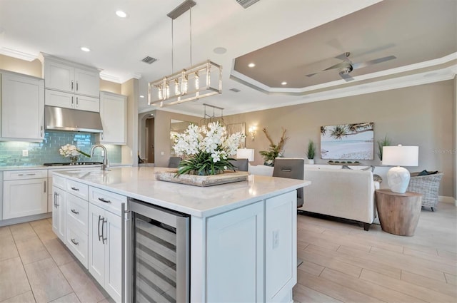 kitchen featuring pendant lighting, a kitchen island with sink, white cabinets, wine cooler, and ceiling fan