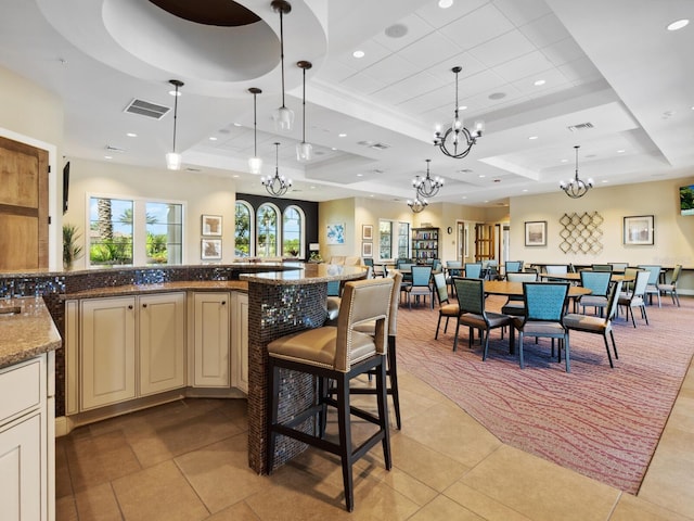 kitchen with light tile patterned floors, hanging light fixtures, a kitchen breakfast bar, dark stone countertops, and a tray ceiling