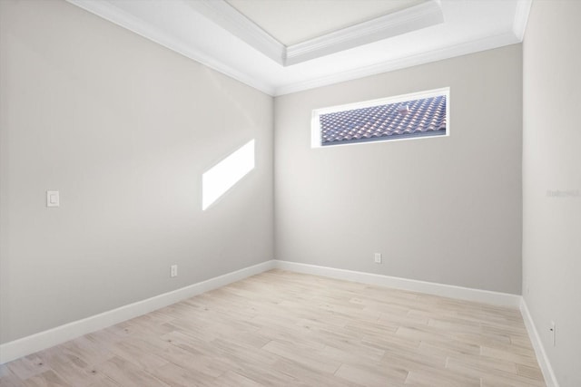 empty room with a raised ceiling, light hardwood / wood-style floors, and ornamental molding