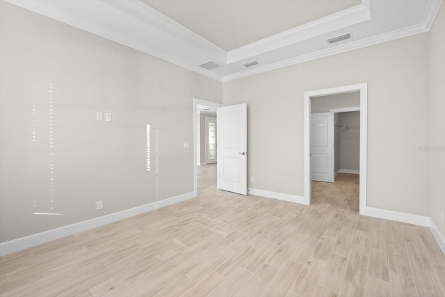 unfurnished bedroom with a raised ceiling, light wood-type flooring, a spacious closet, and crown molding