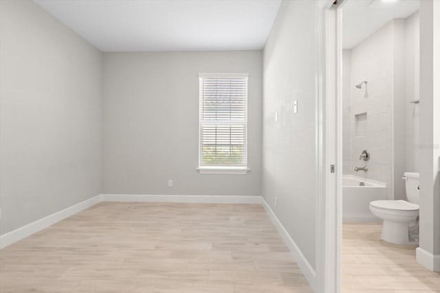 interior space with bathtub / shower combination, hardwood / wood-style floors, and toilet