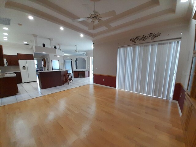 kitchen featuring dark brown cabinetry, a breakfast bar area, white refrigerator with ice dispenser, an island with sink, and light wood-type flooring