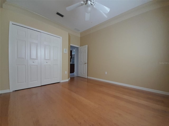 unfurnished bedroom with hardwood / wood-style flooring, ceiling fan, crown molding, and a closet