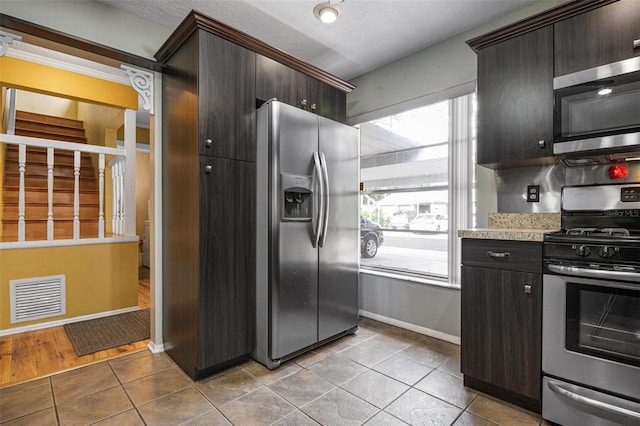 kitchen with dark brown cabinetry, light tile patterned floors, stainless steel appliances, and a textured ceiling