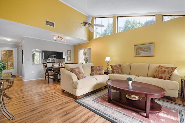 living room with a healthy amount of sunlight, light wood-type flooring, ceiling fan, and ornamental molding