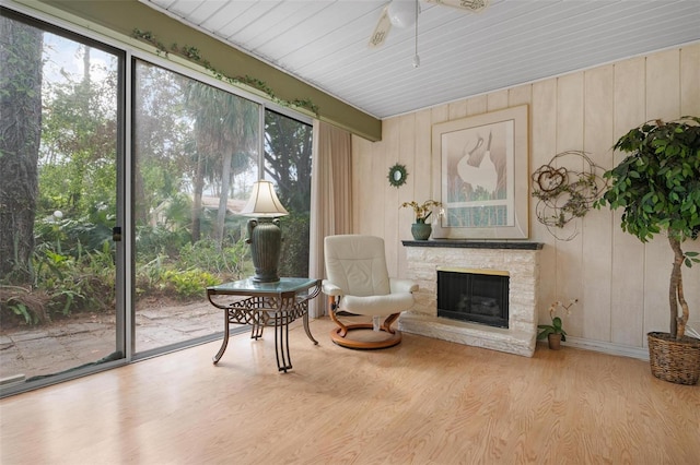 sitting room featuring hardwood / wood-style flooring, a stone fireplace, ceiling fan, and wood walls