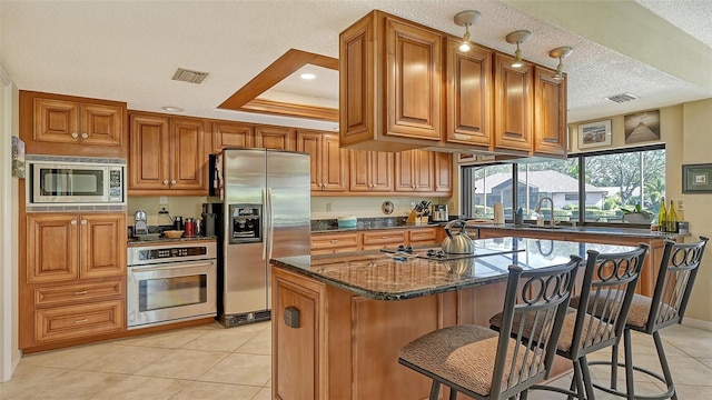 kitchen featuring appliances with stainless steel finishes, a center island, a kitchen bar, dark stone countertops, and a tray ceiling