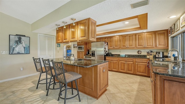 kitchen with stainless steel appliances, a raised ceiling, dark stone countertops, a kitchen island, and sink