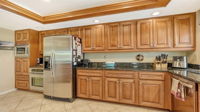 kitchen featuring appliances with stainless steel finishes, dark stone counters, crown molding, and a tray ceiling