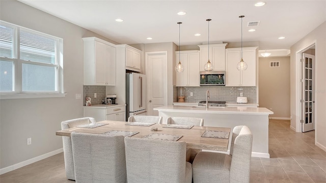 kitchen featuring a center island with sink, white cabinetry, a breakfast bar, appliances with stainless steel finishes, and hanging light fixtures