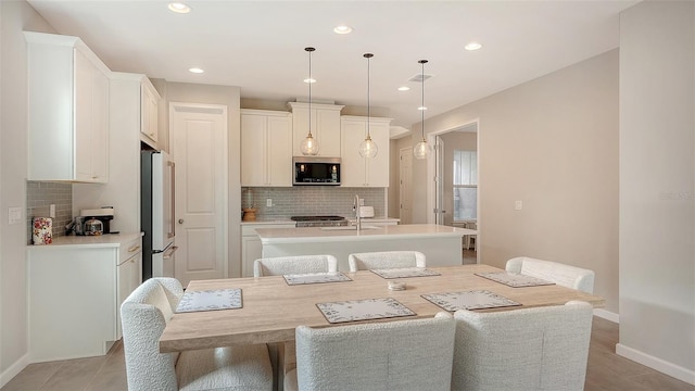 kitchen with hanging light fixtures, a center island with sink, white cabinetry, and appliances with stainless steel finishes