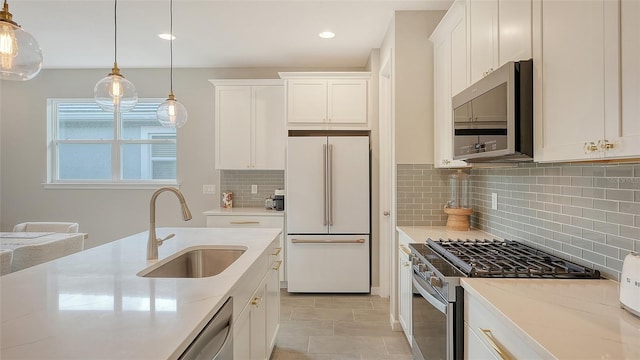 kitchen with stainless steel appliances, pendant lighting, light stone countertops, sink, and white cabinets