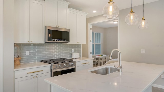 kitchen featuring stainless steel appliances, a center island with sink, white cabinets, hanging light fixtures, and sink