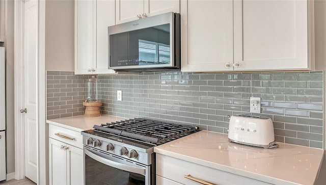 kitchen featuring white cabinets, light stone counters, appliances with stainless steel finishes, and backsplash