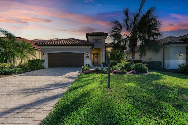 mediterranean / spanish-style home with a garage, a tiled roof, decorative driveway, a lawn, and stucco siding