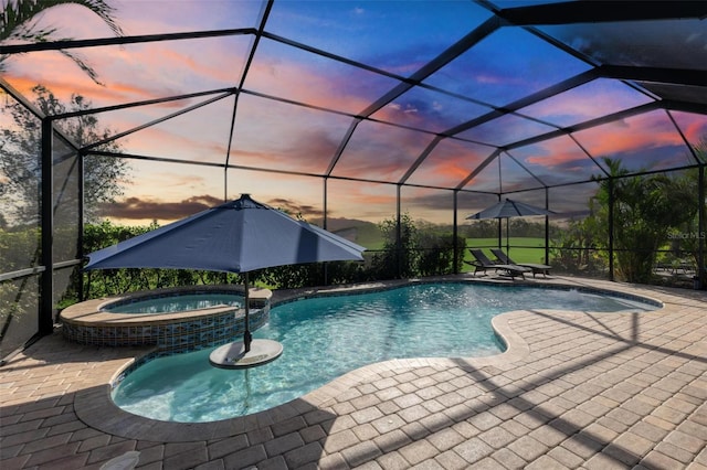 pool at dusk with an in ground hot tub, a patio, and glass enclosure