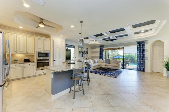 kitchen featuring appliances with stainless steel finishes, light stone counters, a breakfast bar, pendant lighting, and a center island with sink