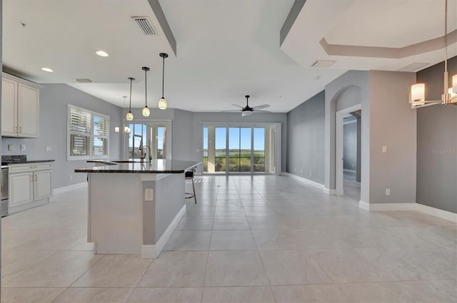 kitchen with a breakfast bar, dark stone countertops, ceiling fan with notable chandelier, an island with sink, and hanging light fixtures