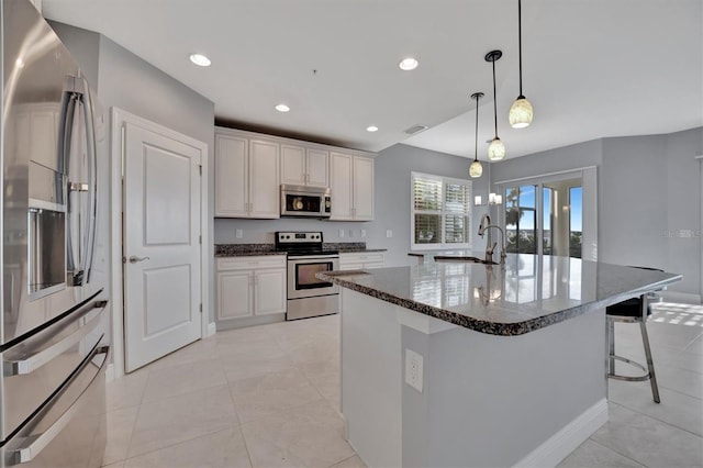 kitchen featuring stainless steel appliances, white cabinetry, sink, decorative light fixtures, and an island with sink