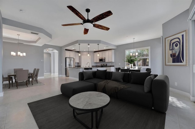 living room featuring ceiling fan with notable chandelier, light tile patterned floors, sink, and a tray ceiling