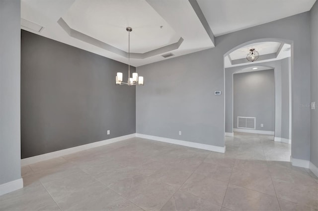 spare room with a tray ceiling and a notable chandelier