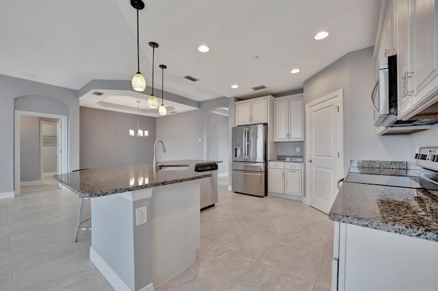 kitchen with stainless steel appliances, white cabinetry, sink, decorative light fixtures, and a kitchen island with sink