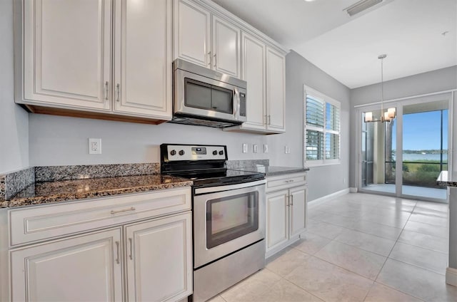 kitchen with stainless steel appliances, dark stone counters, a notable chandelier, light tile patterned floors, and white cabinets