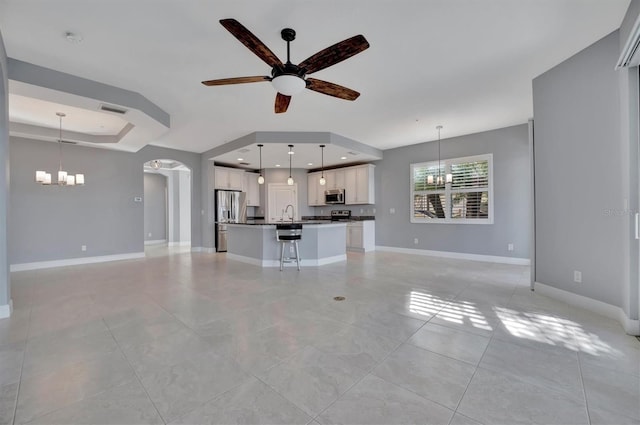 unfurnished living room with ceiling fan with notable chandelier and a raised ceiling