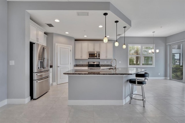 kitchen with dark stone countertops, white cabinetry, a kitchen island with sink, and appliances with stainless steel finishes