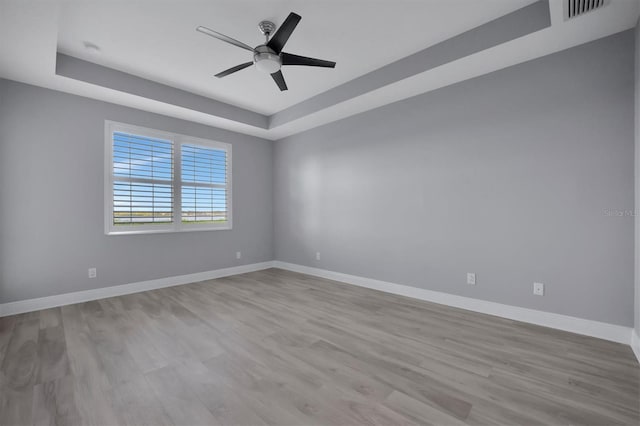 unfurnished room with light hardwood / wood-style floors, ceiling fan, and a raised ceiling