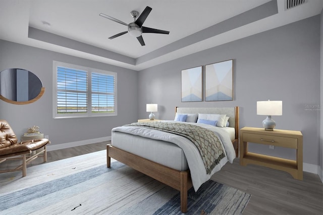 bedroom with hardwood / wood-style floors, ceiling fan, and a tray ceiling