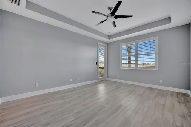 spare room featuring light hardwood / wood-style floors, ceiling fan, and a tray ceiling