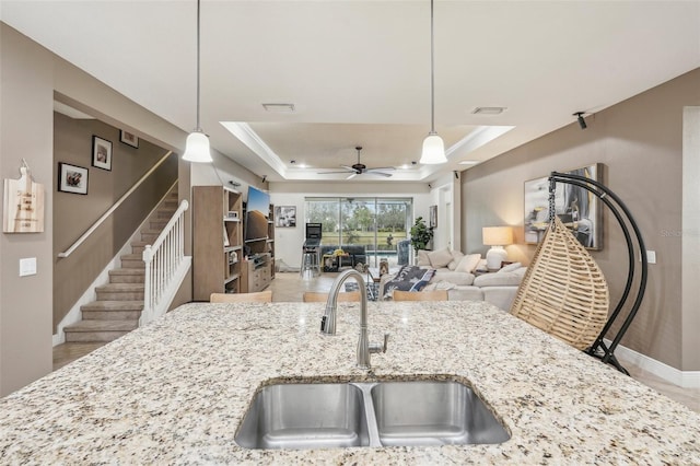 kitchen featuring light stone counters, a raised ceiling, ceiling fan, sink, and hanging light fixtures