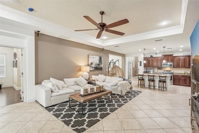 tiled living room featuring a tray ceiling, ceiling fan, and ornamental molding