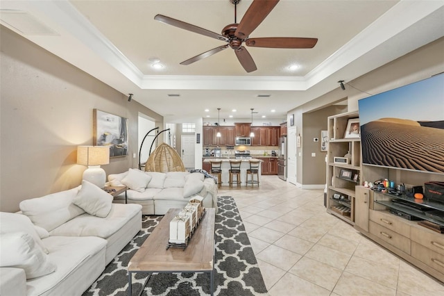 living room featuring a tray ceiling, ceiling fan, light tile patterned floors, and ornamental molding