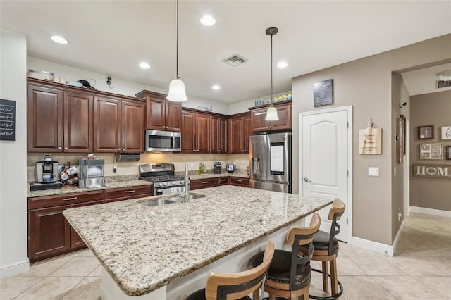 kitchen featuring pendant lighting, a kitchen breakfast bar, an island with sink, and appliances with stainless steel finishes