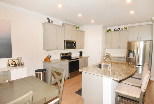 kitchen with a kitchen island with sink, sink, light stone countertops, appliances with stainless steel finishes, and light hardwood / wood-style floors