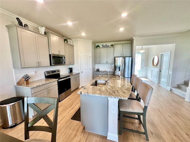 kitchen with sink, light wood-type flooring, stainless steel appliances, and an island with sink