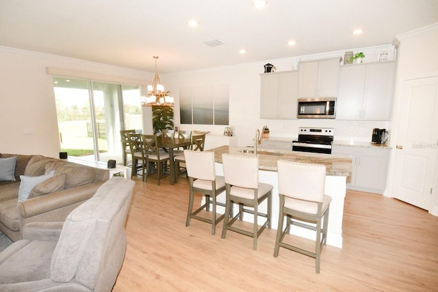 kitchen featuring a center island with sink, sink, hanging light fixtures, white cabinetry, and stainless steel appliances