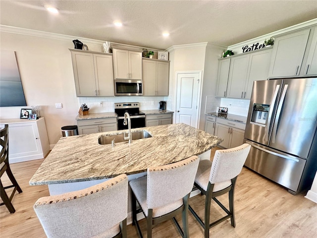 kitchen with appliances with stainless steel finishes, gray cabinetry, a kitchen island with sink, sink, and light hardwood / wood-style floors