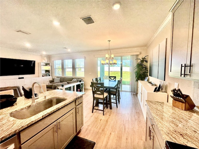 kitchen featuring light wood-type flooring, light stone counters, crown molding, sink, and a chandelier