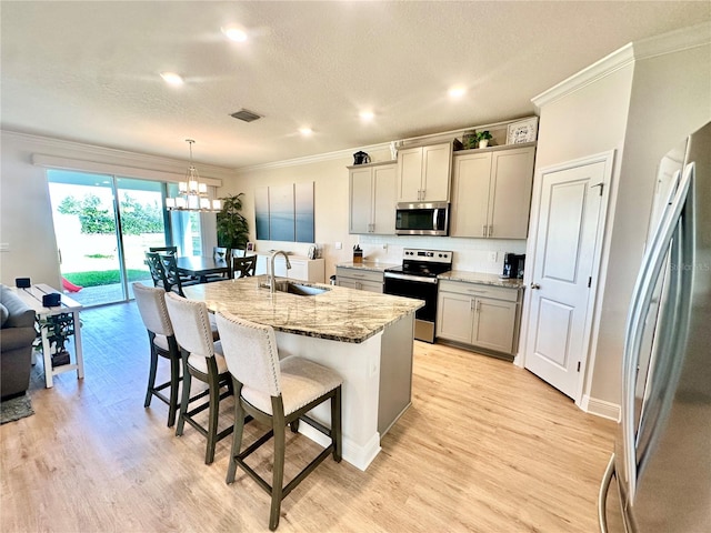 kitchen with appliances with stainless steel finishes, sink, decorative light fixtures, gray cabinets, and an island with sink