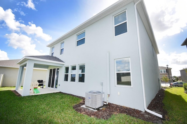 rear view of property with central AC, a patio area, and a lawn